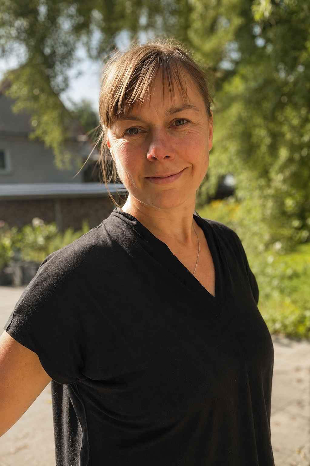 Ulrike Grey lächelt in einem grünen Garten ruhig in die Kamera.